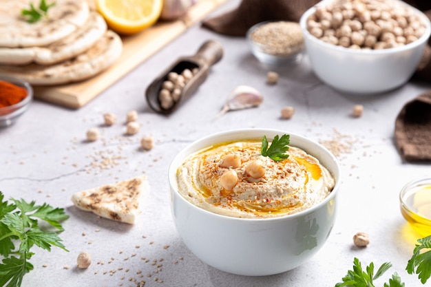 Photo classic hummus in a bowl with ingredients on  light background.