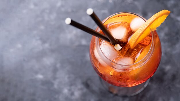 Classic italian aperitif aperol spritz cocktail in glass with slice of orange on dark wall, top view