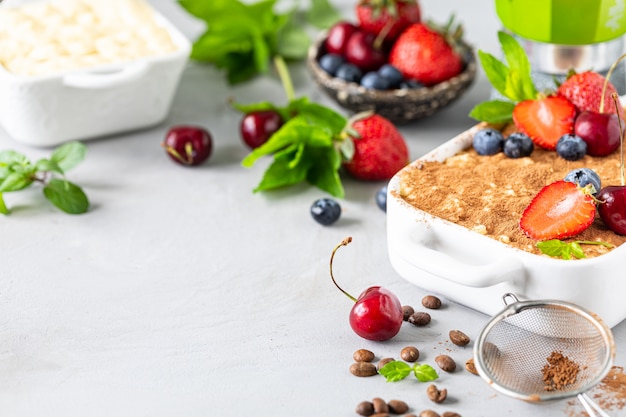 Classic Italian dessert Tiramisu decorated with strawberries, cherries and mint on a white background. Copy space for your text.