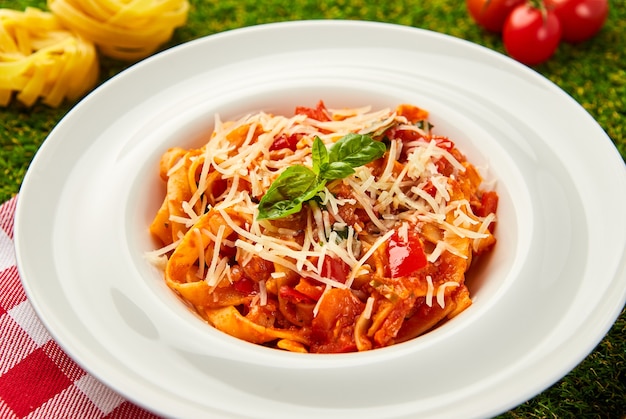 Classic italian pasta arrabbiata with basil and freshly parmesan cheese on a green grass