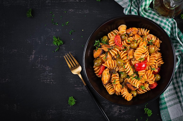 Classic italian pasta fusilli marinara with mussels green olives and capers on dark table Fusilli pasta with sauce marinara Top view overhead