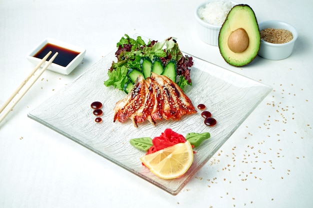 Classic Japanese sashimi - raw eel with salad on a white plate in a composition with ingredients