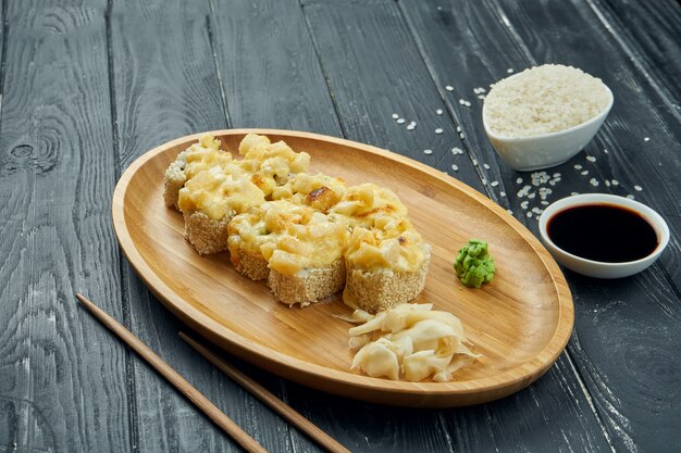 Classic japanese sushi rolls - baked rolls with cream cheese, spicy sauce and chicken on a bamboo plate on a black wooden background