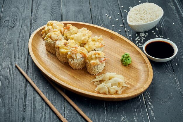 Classic japanese sushi rolls - baked rolls with cream cheese, spicy sauce and shrimp on a bamboo plate on a black wooden background