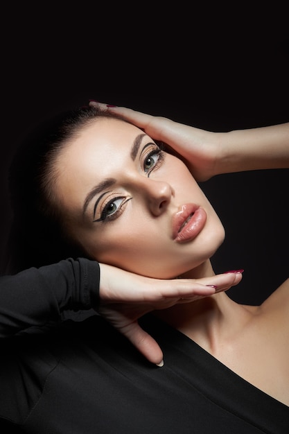 Classic makeup on woman face, beautiful big eyes. Fashion Perfect makeup, expressive eyes on girl face, smooth black eyebrows, licked brunette hair. Portrait woman on dark background