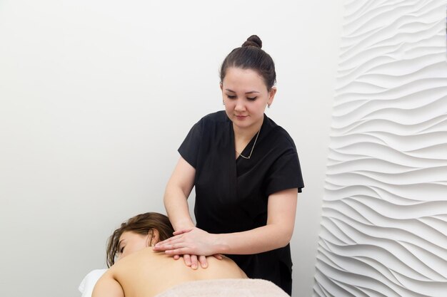 Foto massaggio classico nel salone di bellezza della spa giovane massaggiatrice vestito nero