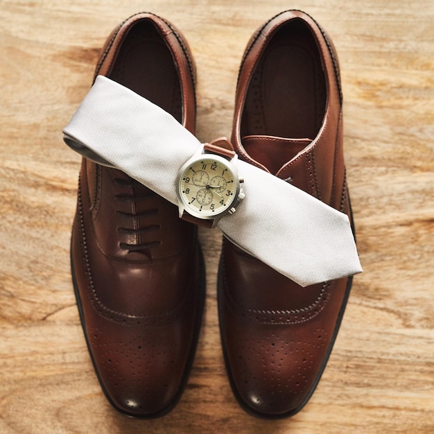 Photo classic never goes out of fashion still life shot of a wristwatch and tie on top of formal shoes on a wooden surface