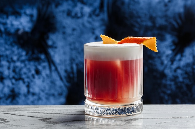 Photo classic old fashioned red cocktail in a retro glass with ice and orange peel on a blue background top view