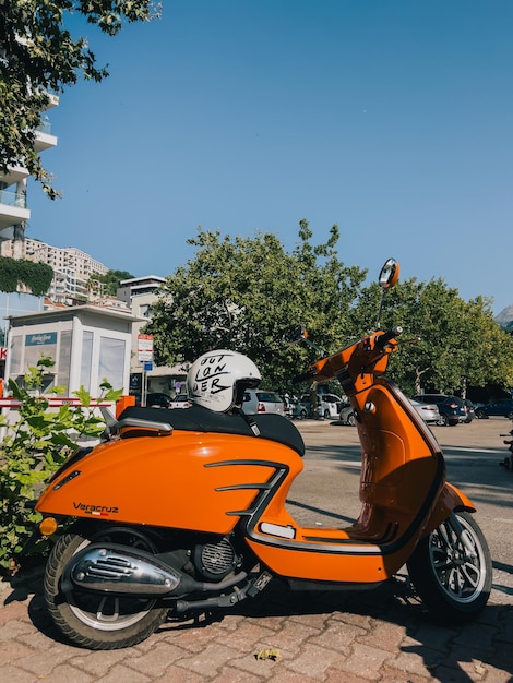 座席にヘルメットをかぶったクラシックなオレンジ色のモペットが建物近くの駐車場に立っています