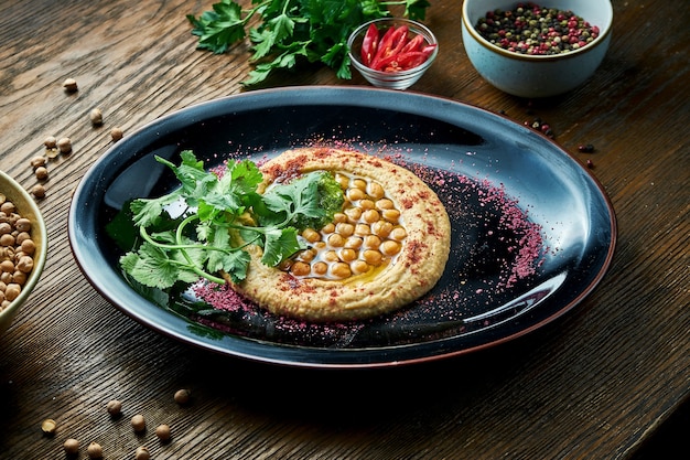 A classic oriental appetizer dish - chickpea hummus with white olive oil, served on a black plate on a wooden table. Restaurant food