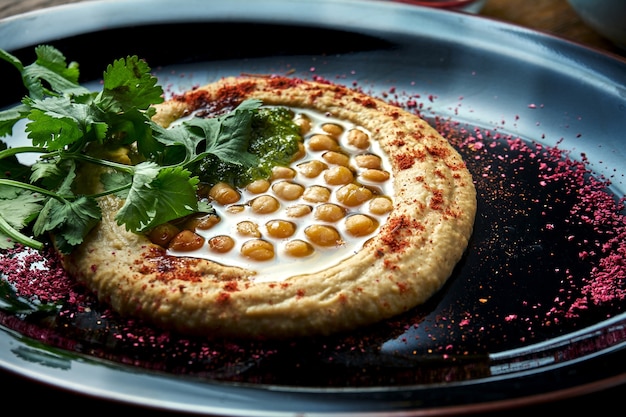 A classic oriental appetizer dish - chickpea hummus with white olive oil, served on a black plate on a wooden table. Restaurant food