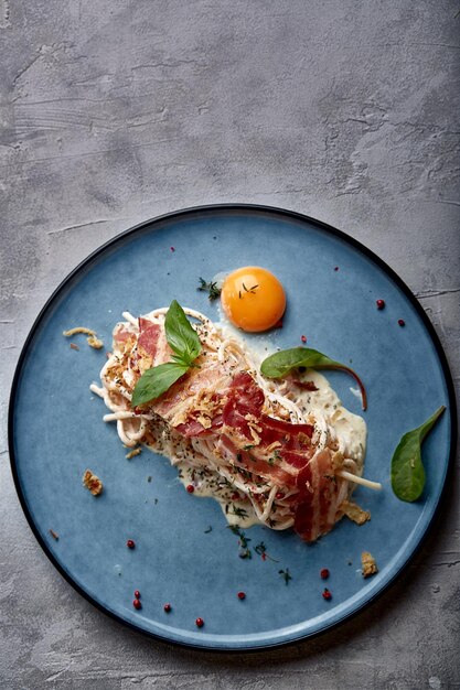 Classic pasta carbonara with yolk on a plate Pasta laid out on a blue plate on a dark background Concept of Italian cuisine beautiful serving dishes closeup