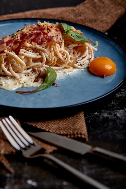 Classic pasta carbonara with yolk on a plate. Pasta laid out on a blue plate on a dark surface. Concept of Italian cuisine, beautiful serving dishes, close-up.