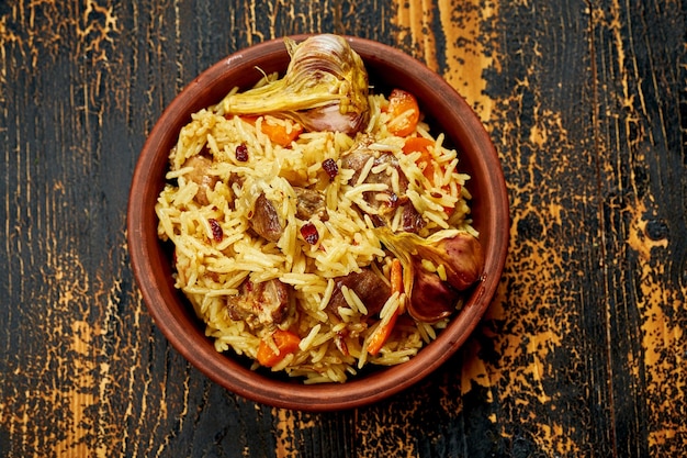 Classic pilaf with beef garlic and carrots in a clay plate on a wooden background Rustic