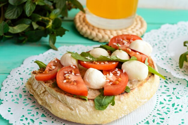Classic sandwich with mozzarella, fresh tomatoes, arugula and sesame seeds on toast. Breakfast.