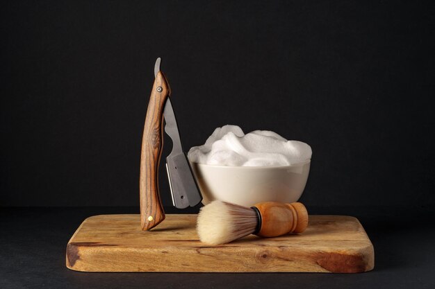 Classic shaving equipment with razor brush and soap on wooden stand against dark background