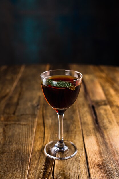 A classic sour cocktail in a nick and nora glass garnished with a mint leaf on wooden table