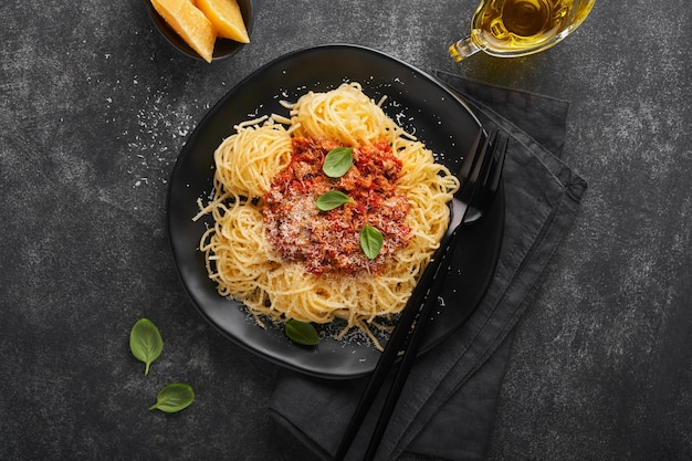 Classic spaghetti pasta bolognese tasty appetizing italian\
spaghetti with bolognese sauce tomato sauce cheese parmesan and\
basil on black plate on dark stone or concrete table background top\
view