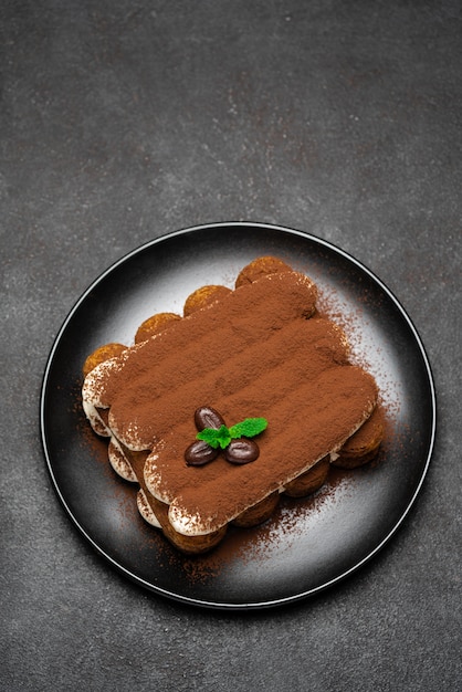 Classic tiramisu dessert on ceramic plate on dark concrete background