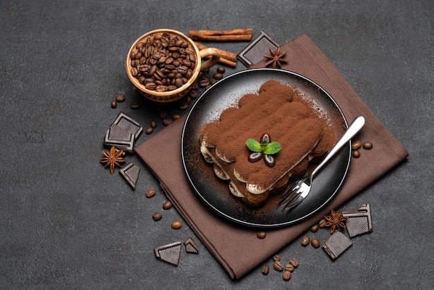 Classic tiramisu dessert on a ceramic plate on dark concrete background