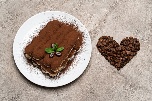 Классический десерт тирамису на керамической тарелке и кофейные зерна в форме сердца