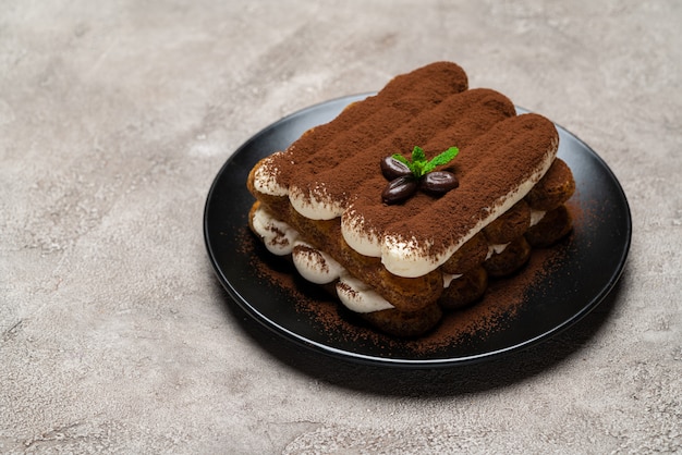 Classic tiramisu dessert on ceramic plate on light grey concrete surface