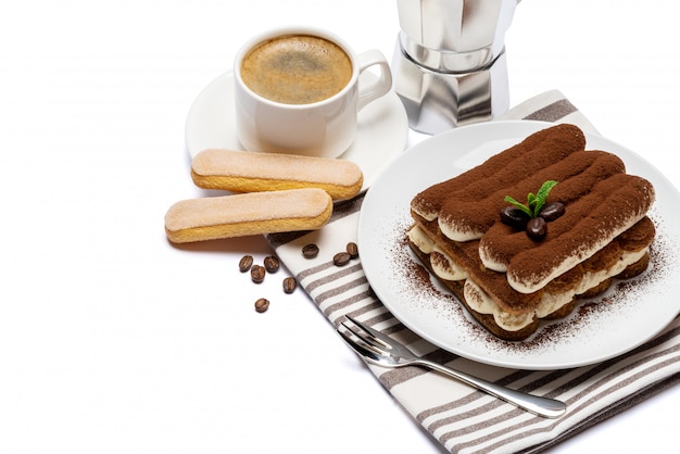 Classic tiramisu dessert on ceramic plate, savoiardi cookies and cup of coffee isolated on white surface with clipping path