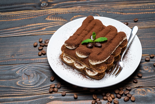 Classic tiramisu dessert on ceramic plate on wooden background