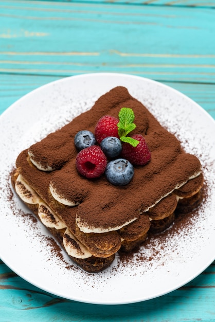 Classic tiramisu dessert with raspberries and blueberries on blue wooden table