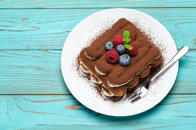 Classic tiramisu dessert with raspberries and blueberries on blue wooden table