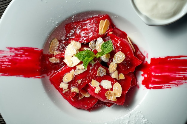 Classic Ukrainian Pierogi or Varenyky with cherries, red sauce, sour cream and almonds in a white plate.