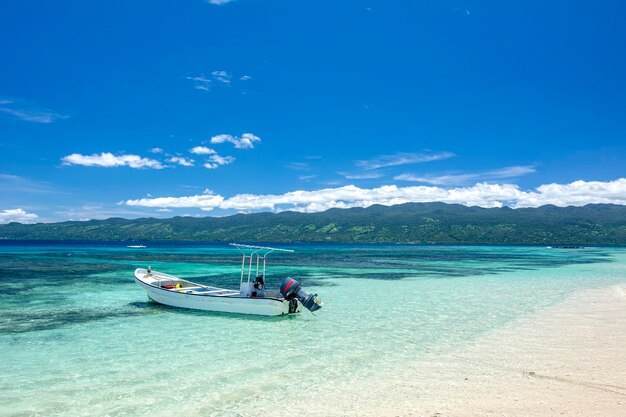 写真 透き通った水と白い砂浜の海岸線に浮かぶボートのある、熱帯のビーチシーンの古典的な眺め