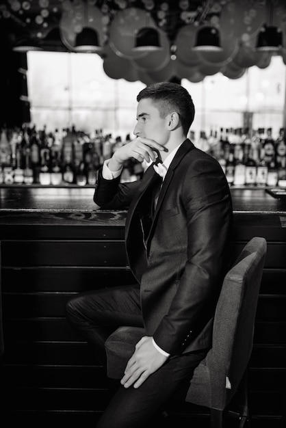 Classic wedding photo. Portrait of a groom sitting on a chair by the bar. Low key.