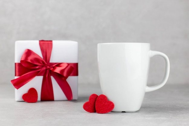 Classic white mug mockup with red hearts and gift box on light gray concrete surface