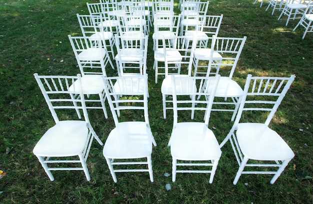 装飾のない緑の芝生の上の古典的な白い結婚式の椅子夏