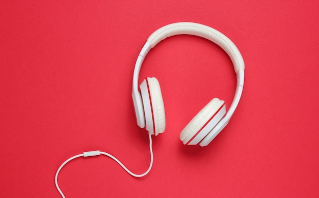 Classic white wired headphones on red paper background. Retro style. 80s. Pop culture. Music lover. Top view