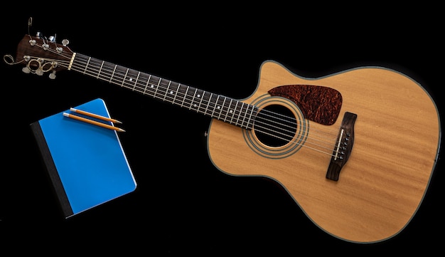 Classical acoustic guitar and blue notepad on black background, top view, musical creativity concept.