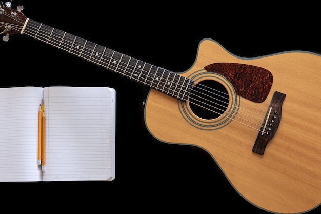 Classical acoustic guitar, open notepad on a black background, top view.