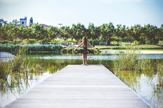 Classical ballerina posing on a footbridge of an urban lake on a sunny day