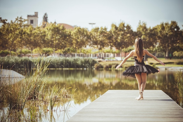 Classical ballerina posing on a footbridge of an urban lake on a sunny day