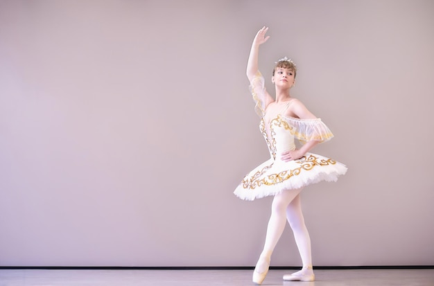 スタジオのクラシックバレエダンサーは、チュチュスカートのtiptoeyoung美しい優雅な白人バレリーナ練習バレエの位置に立っています