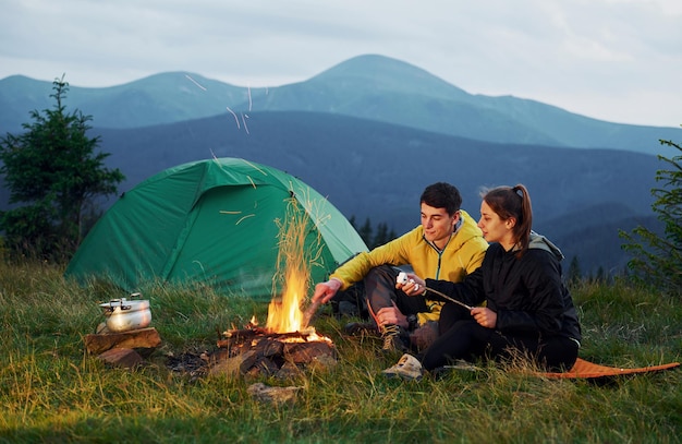 Classical marshmallow making near campfire Young couple Majestic Carpathian Mountains Beautiful landscape of untouched nature