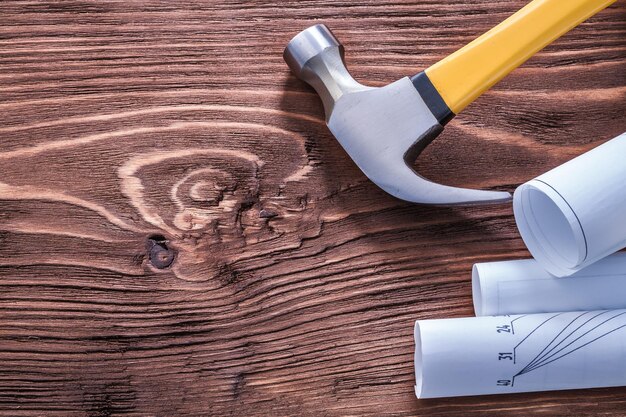 Claw hammer and blueprints on brown vintage wooden board construction concept