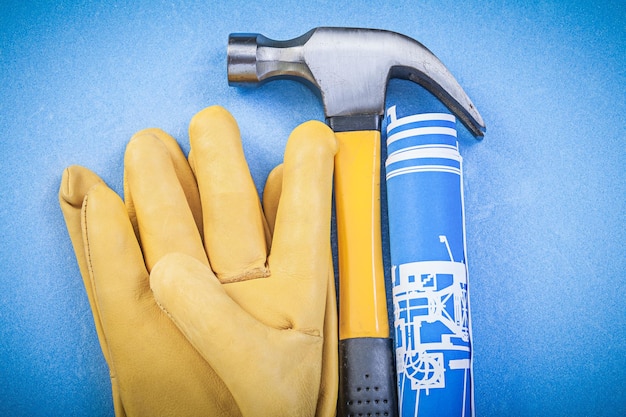 Claw hammer protective gloves rolled up construction drawings on blue background