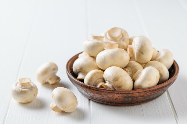 Clay bowl filled with fresh mushrooms on a white wooden table