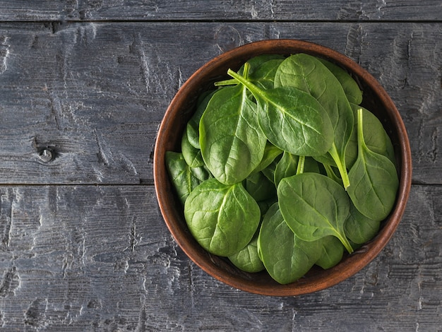 A clay bowl filled with spinach leaves on a black wooden table. Food for fitness. Vegetarian food. The view from the top.