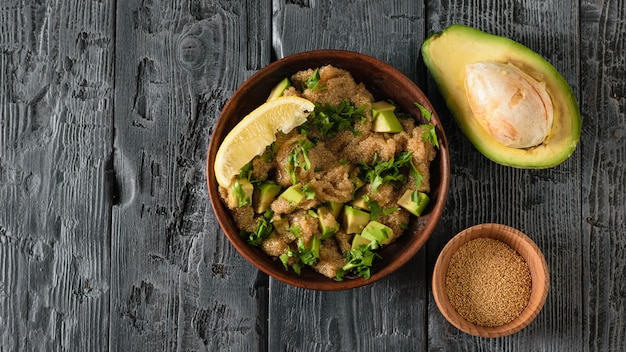 Clay bowl with amaranth seed salad with avocado, lemon and parsley and bowl with amaranth on a dark wooden table