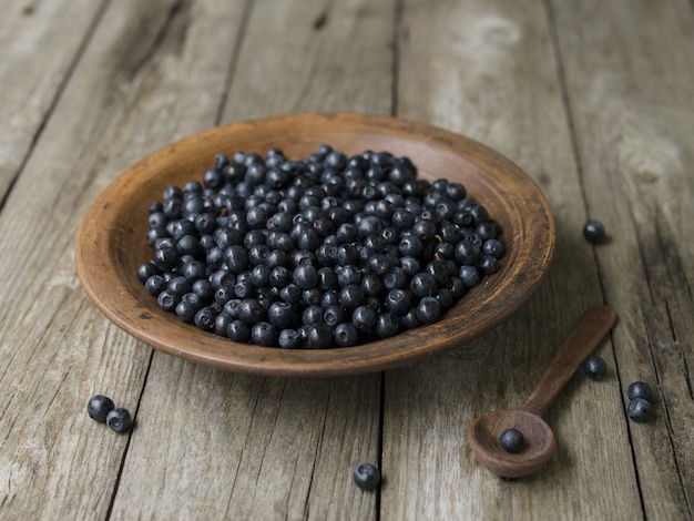 Ciotola dell'argilla con i mirtilli su una vecchia tavola di legno. bacche appena colte. superfood antiossidante del mirtillo, concetto per il cibo sano.