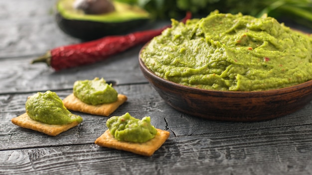 Ciotola di argilla con guacamole fresco, pomodori, limone, patatine, avocado e aglio sul tavolo di legno