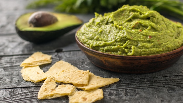 Clay bowl with freshly made guacamole and pieces of Mexican tortilla on a wooden table